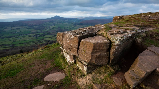 A pile of rocks marking the summit of the Skirrid with far reaching views across to the peak of Sugar Loaf mountain beyond